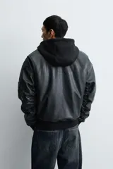 Cazadora estilo bomber de corte relajado confeccionada en tejido efecto piel color negro. Presenta capucha integrada, cierre frontal de cremallera, bolsillos laterales de vivo y puños y bajo con acabado en rib. El interior cuenta con forro acolchado en color naranja.