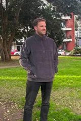 Buzo de pana gris oscuro con cuello alto y cierre frontal parcial de cuarto. Posee bolsillos frontales tipo canguro y diseño holgado de manga larga.