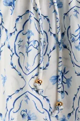 Blusa en mezcla de viscosa con peplum acampanado, cuello redondo, escote en V y tiras finas con cuentas decorativas. Presenta mangas globo largas con elástico en los puños y un estampado en tonos blancos y azules con motivos florales y geométricos.
