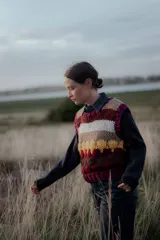 Chaleco tejido de punto con diseño de rayas horizontales y bloques de color en tonos bordó, beige, blanco y amarillo. Presenta cuello redondo y terminaciones acanaladas.