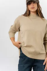 Sweater de tejido de punto color marrón, con cuello alto, corte relajado y terminaciones en rib en puños y cintura. Presenta una hilera de botones metálicos decorativos en uno de los laterales.