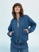 Campera bomber de denim azul con cierre frontal, bolsillos laterales y elástico en puños y cintura.