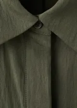 Vestido largo verde militar, con cuello camisero, cierre frontal con botones, mangas tres cuartos y diseño evasé. Incluye un cinturón fino de poliuretano con hebilla metálica.