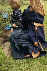 Pantalón de corte amplio con estampado de cuadros escoceses en tonos azul y verde. Presenta apliques de tela plisada con costuras decorativas en zigzag a lo largo de las piernas, tajos laterales y bolsillos funcionales.