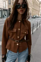 Blazer de cuello redondo y manga larga, confeccionado en tejido efecto ante. Presenta cierre frontal con botones, bolsillos con tapeta en el pecho y cinturón ajustable en la cintura.