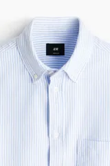 Camisa de algodón H&M Oxford con estampado de rayas verticales celestes y blancas, cuello americano, bolsillo en el pecho y manga larga.