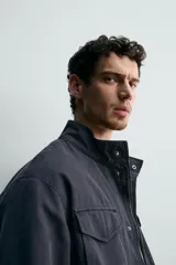 Cazadora regular fit de algodón color gris oscuro con efecto lavado, cuello subido, manga larga y cierre frontal con cremallera oculta por solapa con botones a presión. Cuenta con cuatro bolsillos frontales de plastrón con solapa y cintura ajustable con cordón interior.