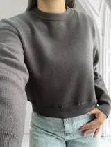 Sweater gris oscuro de corte cropped, con cuello redondo y mangas largas.