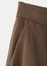 Pantalón de corte recto y tiro regular, color marrón, con bolsillos laterales y traseros con ribete. Cierre frontal con cremallera, botón y ganchos ocultos.