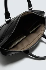 Maletín negro con textura grabada, diseño estructurado y asas de mano. Cuenta con cierre principal de cremallera, bolsillo frontal plano y bolsillo interior para dispositivos electrónicos de hasta 13 pulgadas. Incluye asa de hombro ajustable y extraíble.