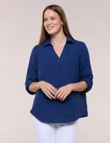 Blusa verde de calce holgado y caída fluida, confeccionada en tejido tipo crepé. Cuenta con cuello camisero con solapa, escote en V y cierre parcial al frente con tres botones metálicos. Las mangas son largas con puños abotonados.
