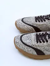 Championes urbanos de diseño exclusivo con paneles en cuero negro y textil estampado con motivo animal print de puntos. Presenta una suela de plataforma en tono marrón con relieve dentado y detalles en cuero beige en el talón.