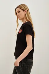 Remera negra de algodón con cuello redondo y manga corta. Presenta un aplique bordado en el pecho con forma de corazón rojo que contiene un ojo detallado con mostacillas y bordados.