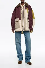 Abrigo acolchado de corte recto con diseño patchwork en tonos burdeos, beige y verde oliva. Presenta cuello camisero de pana, cierre frontal con botones de presión, bolsillos de tapeta en el bajo y bolsillos de vivo en el pecho.