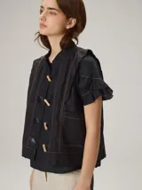 Chaleco negro con diseño de alamares frontales, costuras a la vista en contraste y volados en los hombros.