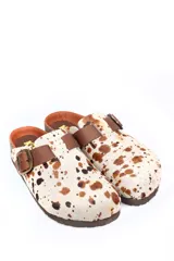 Zueco de cuero con estampa tipo animal print de vaca, con tira de ajuste marrón y hebilla metálica. Plantilla anatómica y suela de corcho y goma.