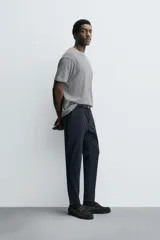 Pantalón de corte slim fit y color negro, confeccionado en tejido elástico. Cuenta con cintura elástica, trabillas, bolsillos frontales y cierre con cremallera y botón.