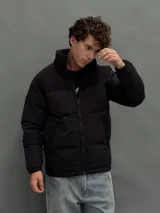 Campera puffer negra con diseño de paneles, cierre frontal completo y cuello alto. Presenta una textura diferenciada en la parte superior y bolsillos laterales.