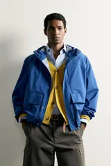 Cazadora técnica relaxed fit de color azul, con cuello subido, capucha ajustable, bolsillos frontales de plastrón con solapa, cierre de cremallera oculta y puños elásticos.