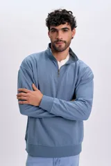 Buzo deportivo color azul piedra, con cuello alto, cierre frontal parcial y mangas largas con puños elásticos.