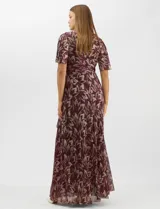 Vestido largo de fiesta con diseño cruzado, escote en V y drapeado lateral en la cintura. Presenta mangas cortas acampanadas y falda amplia con caída fluida. Confeccionado en tejido liviano con acabado plisado y estampado floral metalizado.
