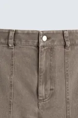 Pantalón de corte relajado en color marrón con efecto lavado. Presenta bolsillos frontales tipo cargo, cierre con cremallera y botón, y una línea horizontal de tachas metálicas a tono en la parte superior de las piernas.