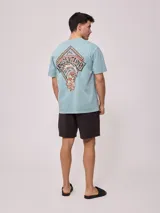 Remera holgada de algodón color beige, de manga corta y cuello redondo, con un gran estampado colorido en la espalda con diseño de olas y la inscripción 'Rusty Tribe'.