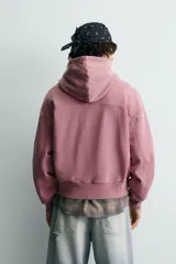 Sudadera tipo hoodie con cierre frontal de cremallera, diseño boxy fit, capucha ajustable con cordones, mangas largas con puños elásticos y bolsillos laterales. Presenta un acabado con efecto lavado.