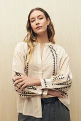 Camisa de lino color beige con bordados geométricos en color negro. Presenta cuello mao, cierre frontal con botones, mangas largas con volumen y puños ajustados.