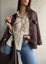 Camisa beige de tejido liviano y calce relajado, con manga larga y detalle de puntilla y bordado en contraste que recorre el frente.