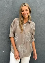 Camisa de seda color visón con bordados en relieve de hojas grandes, cuello camisero, mangas largas y cierre frontal con botones.