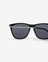 Lentes de sol unisex de la colección Paula X Hawkers, con montura cuadrada negra y patillas plateadas.