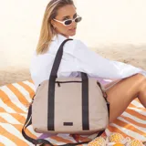Bolso deportivo color gris topo con asas y correa ajustable negras, cuenta con compartimento principal con cierre y bolsillo frontal con cierre.