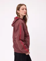 Campera rompevientos color bordó con cierre frontal, capucha con cordones ajustables y franjas laterales en tono más oscuro. Presenta puños elásticos y bolsillos frontales.