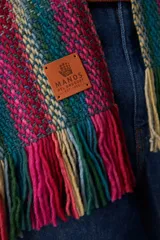 Ruana abierta de tejido de punto con diseño de rayas verticales en tonos fucsia, verde azulado y azul. Presenta terminaciones con flecos en el ruedo y una etiqueta de cuero sintético en el frente.