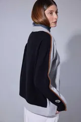 Saco de punto acanalado en color gris claro, con cierre frontal de botones oscuros. Presenta un diseño de bloques de color en las mangas, combinando negro y marrón, y un cuello redondo.