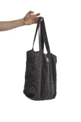 Bolso tipo tote bag de denim negro con diseño acolchado de costuras cuadradas y doble asa superior. Cuenta con un parche ovalado frontal bordado con las letras "dl".