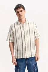 Camisa de manga corta oversize en tejido rústico, con diseño de rayas verticales celestes y blancas, cuello clásico y cierre frontal de botones.