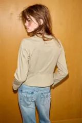 Chaqueta de cuello redondo y manga larga en color beige. Presenta un diseño con doble hilera de botones decorativos en el frente, detalles de encaje a tono y cierre frontal mediante ganchos metálicos ocultos.
