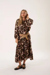 Vestido midi de corte holgado con estampado animal print en tonos marrones y beige. Tiene cuello redondo con lazo, mangas largas abullonadas y falda amplia con volantes. Incluye cinturón marrón con tachas.