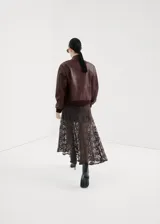 Chaqueta estilo bomber de cuero sintético marrón oscuro, con cierre frontal de cremallera, cuello alto abotonado y bolsillos frontales con solapa.