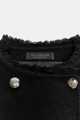 Chaqueta de corte recto confeccionada en mezcla de lana, con cuello redondo y manga larga. Presenta un diseño cruzado con botones metálicos plateados y acabados deshilachados en cuello, puños y ruedo.