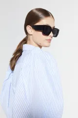 Camisa de algodón a rayas verticales blancas y celestes, con mangas globo muy voluminosas y puños elásticos. Posee cuello camisero clásico y cartera de botones de nácar. El ruedo es más largo en la parte trasera.