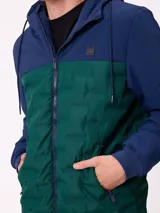 Campera con capucha, diseño bicolor en negro y gris oscuro, con panel frontal acolchado y mangas lisas. Cuenta con cierre frontal, bolsillos laterales y puños elásticos.