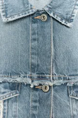 Chaqueta crop de denim azul claro con cuello solapa, manga larga con puño y bolsillos de plastrón con solapa en el pecho. Presenta detalles de costuras deshilachadas y cierre frontal con botones metálicos.