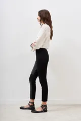 Pantalon negro de corte ajustado, confeccionado en una combinación de materiales que incluye paneles de efecto cuero en la parte frontal y laterales, con diseño de costuras horizontales en las rodillas.