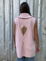 Chaleco de lana merino color rosado, con cuello alto tejido, cierre frontal tipo duffle con botones de madera y detalles en cuero sintético en los bolsillos y cierres.