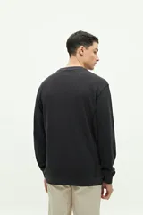 Buzo de felpa gris oscuro, con textura de tejido waffle o gofrado. Presenta cuello redondo, manga larga y un pequeño logo bordado en el pecho.