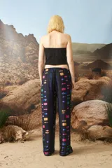 Pantalón de corte holgado y tiro medio, con cintura elástica y cordón de ajuste. Presenta un estampado geométrico multicolor sobre fondo negro.