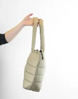 Bolso tipo tote color beige con diseño acolchado y asas tubulares. Presenta el logo de la marca en el centro.